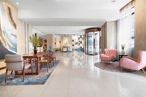 A modern hotel lobby with a dining area, seating, and a glass elevator. - Echarm Hotel (Xiamen)