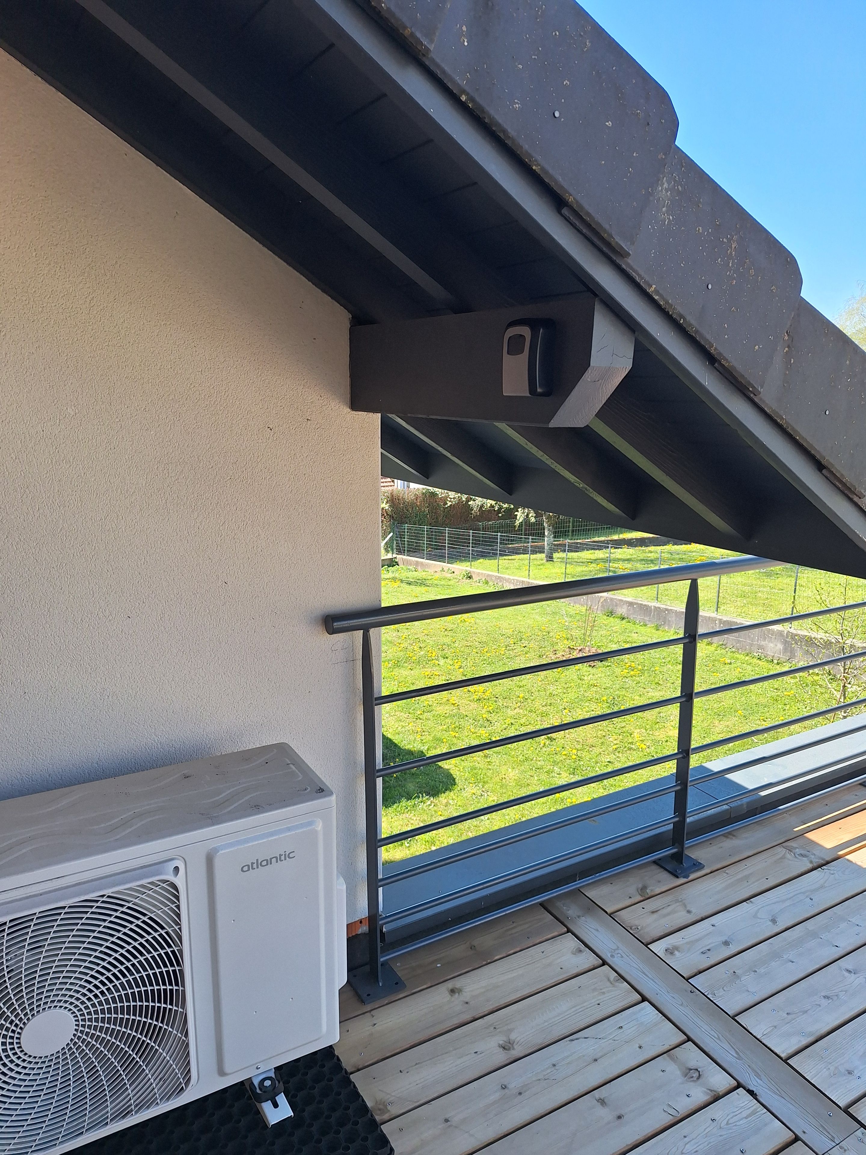 Un balcon donnant sur un espace verdoyant, avec une rambarde en métal et un appareil de climatisation.