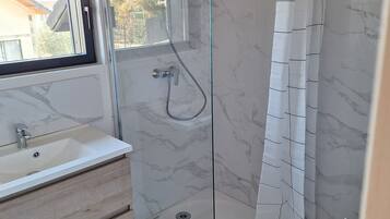 Une salle de bain avec une douche à parois de verre, un lavabo et une fenêtre.