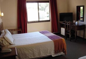 Habitación de hotel con cama, escritorio, silla, televisor y ventana con cortinas.