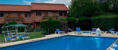A rectangular swimming pool with a clear blue water surface, surrounded by lounge chairs and a covered seating area.