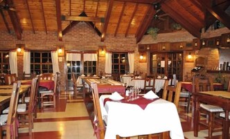 Un restaurante con mesas y sillas de madera, paredes de ladrillo y un techo alto con vigas a la vista.