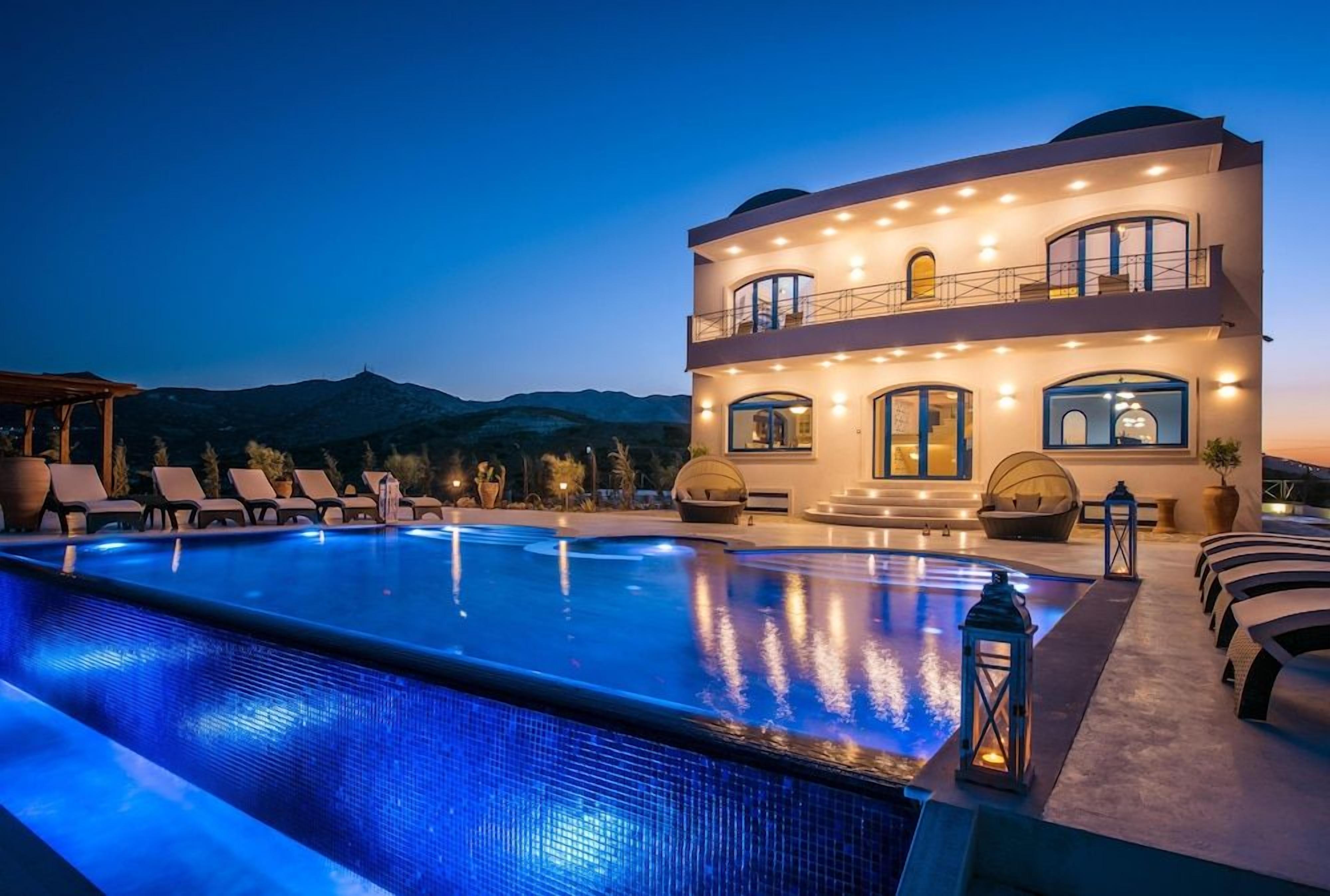 A multi-story hotel with a swimming pool, outdoor seating, and a view of the mountains.