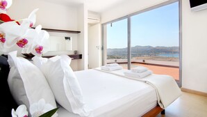 A hotel room with a large bed, a bathroom with a mirror, and a balcony with a view of the landscape.