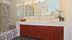 A modern bathroom with a large mirror, white tiles, a shower area, and wooden cabinets.