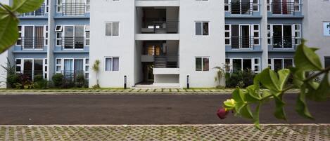 A multi-story residential building with balconies, a central entrance, and a paved walkway.