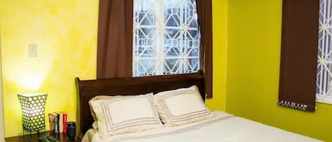 A bedroom with a bed, a nightstand, a lamp, and a window with curtains.