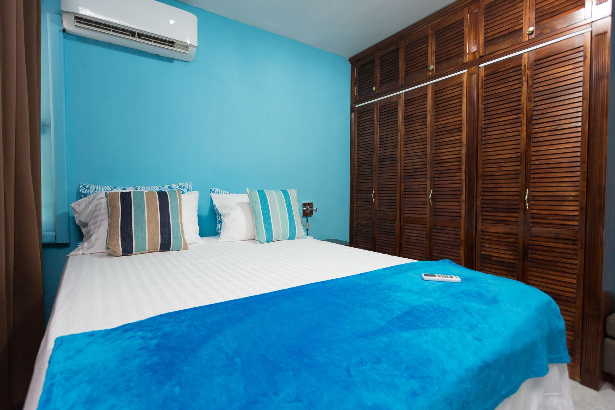 A bedroom with a bed, a blue wall, and a wooden wardrobe.