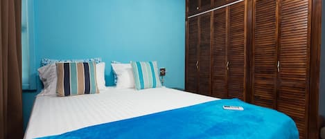 A bedroom with a bed, a blue wall, and a wooden wardrobe.