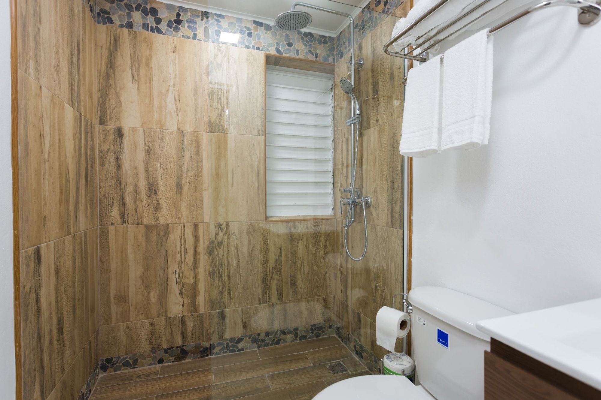 A bathroom with a shower, toilet, and a window with blinds.
