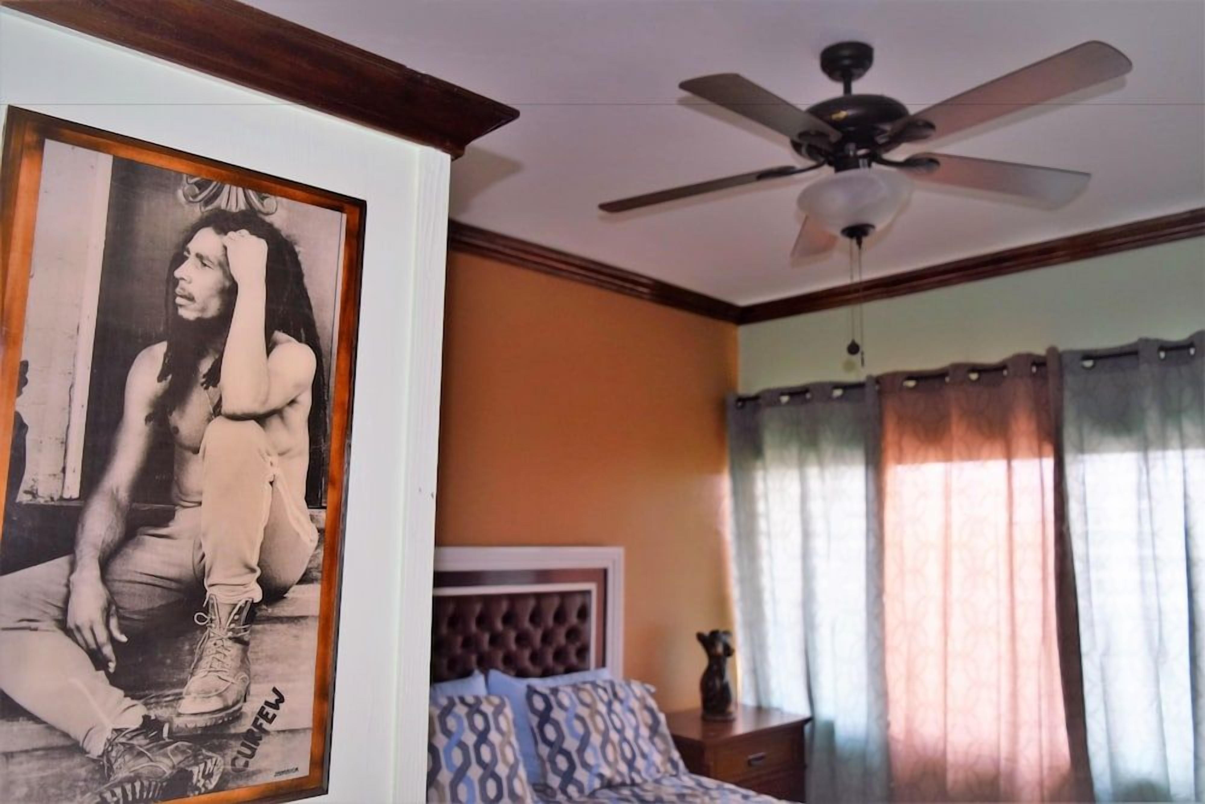 Une chambre à coucher avec un lit, un ventilateur de plafond et un tableau encadré accroché au mur.