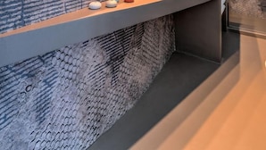 A modern bathroom with a curved vanity, a large mirror, and a textured wall. - The First Riomaggiore 5 Terre (Riomaggiore)