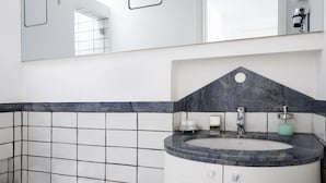 Un bany amb terra de rajola blanca, un lavabo de marbre i un mirall damunt del lavabo.