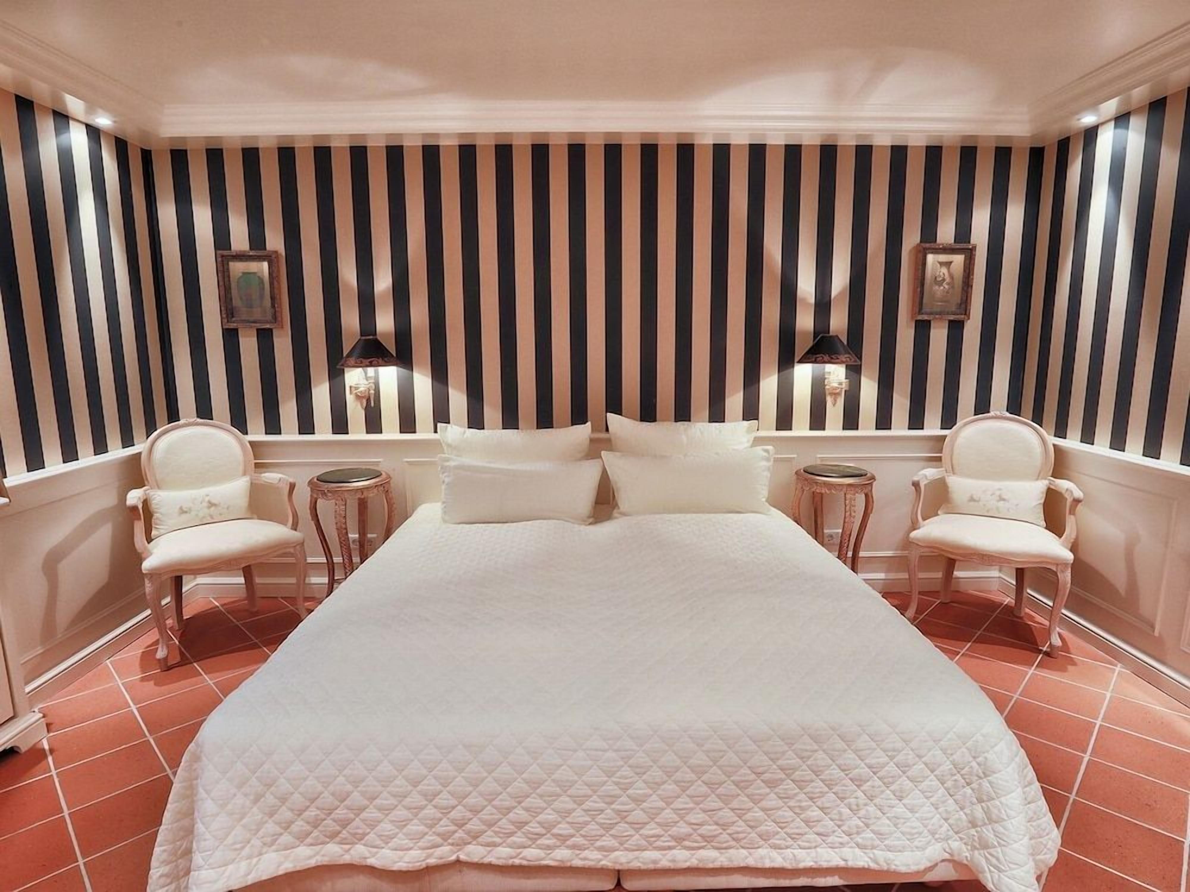 Camera d'albergo con un letto grande, due poltrone, un tavolino rotondo e una parete a righe.