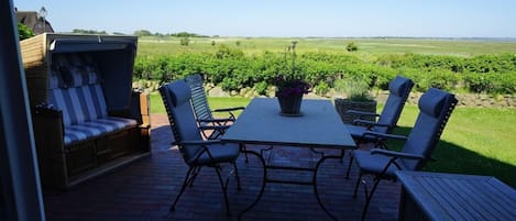 An outdoor patio with a table and chairs, a cushioned seating area, and a view of a vineyard.