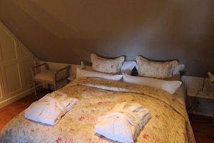 Ein ordentlich gemachtes Bett mit blumigem Bettbezug und zwei Satz Handtücher, ein Sessel und ein Nachttisch mit Lampe.