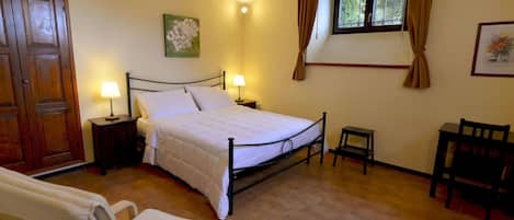Un dormitorio con cama, mesitas de noche, una silla, una ventana con cortinas y una puerta.