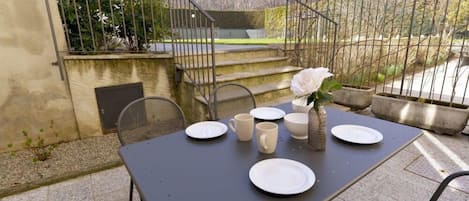 Un patio exterior con una mesa dispuesta para comer, rodeado por una valla de metal y escalones que conducen a un nivel superior.