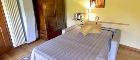 Un dormitorio con una cama, un armario de madera, un radiador y un cuadro en la pared.