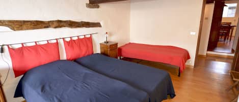Una habitación con dos camas, suelo de madera, un travesaño de madera en el techo y una puerta que da a otra habitación.