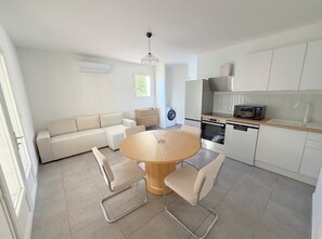 A modern kitchen with a dining area, including a round wooden table and chairs, a built-in oven, and a dishwasher. - 3-Bedroom House - Ocean View - Bastelicaccia (Bastelicaccia)