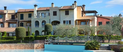 A multi-story hotel with a swimming pool, stone wall, and well-maintained garden.
