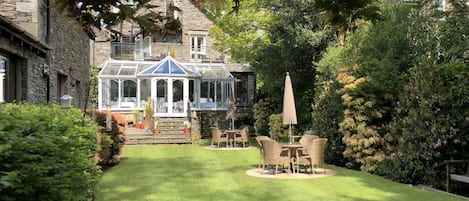 A conservatory with a glass roof, surrounded by a well-maintained lawn and garden.