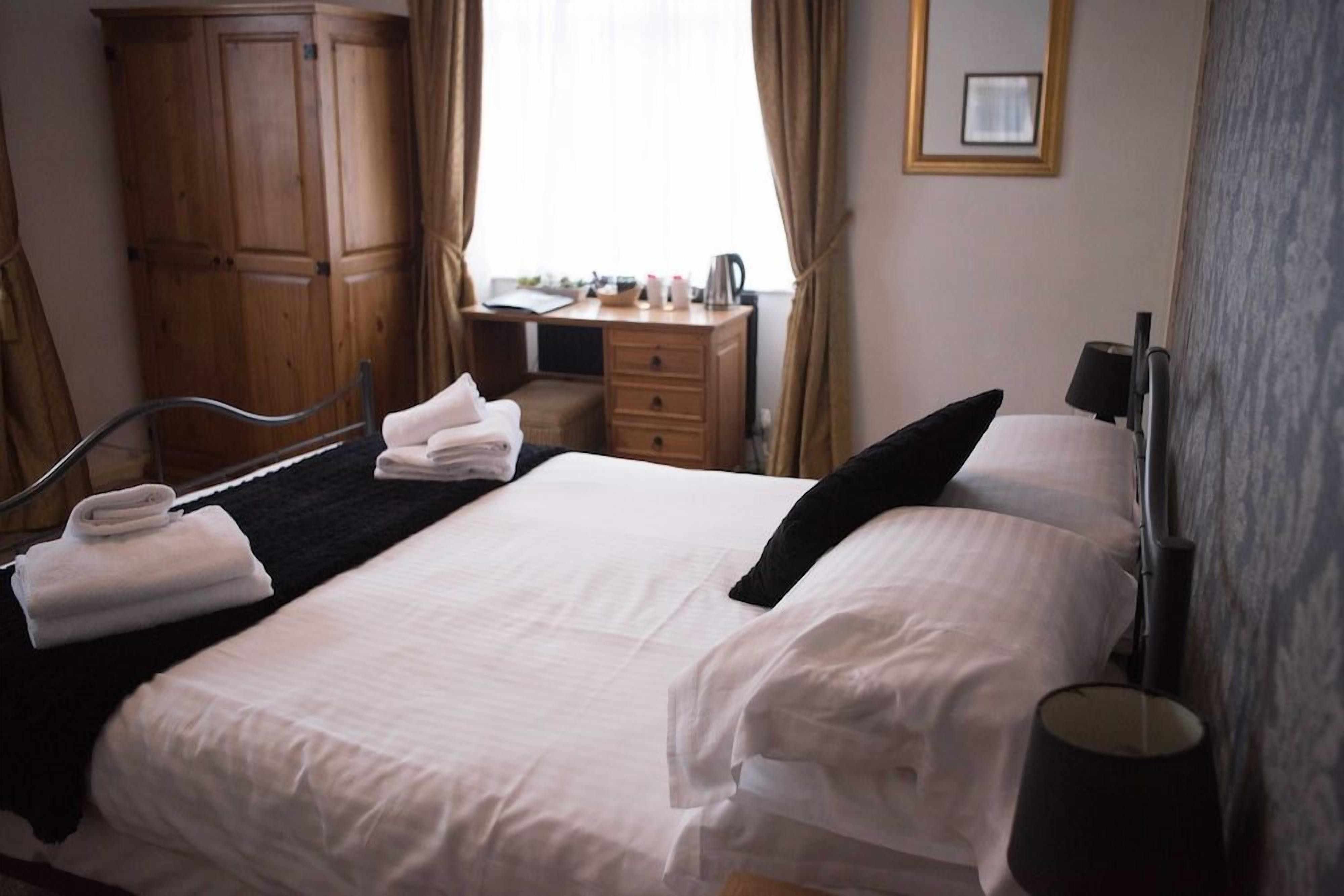 A hotel room with a bed, a desk, a wardrobe, and a window with curtains.