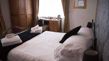 A hotel room with a bed, a desk, a wardrobe, and a window with curtains.