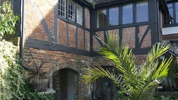 A traditional half-timbered house with a brick archway entrance, a conservatory with glass doors, and a variety of plants.