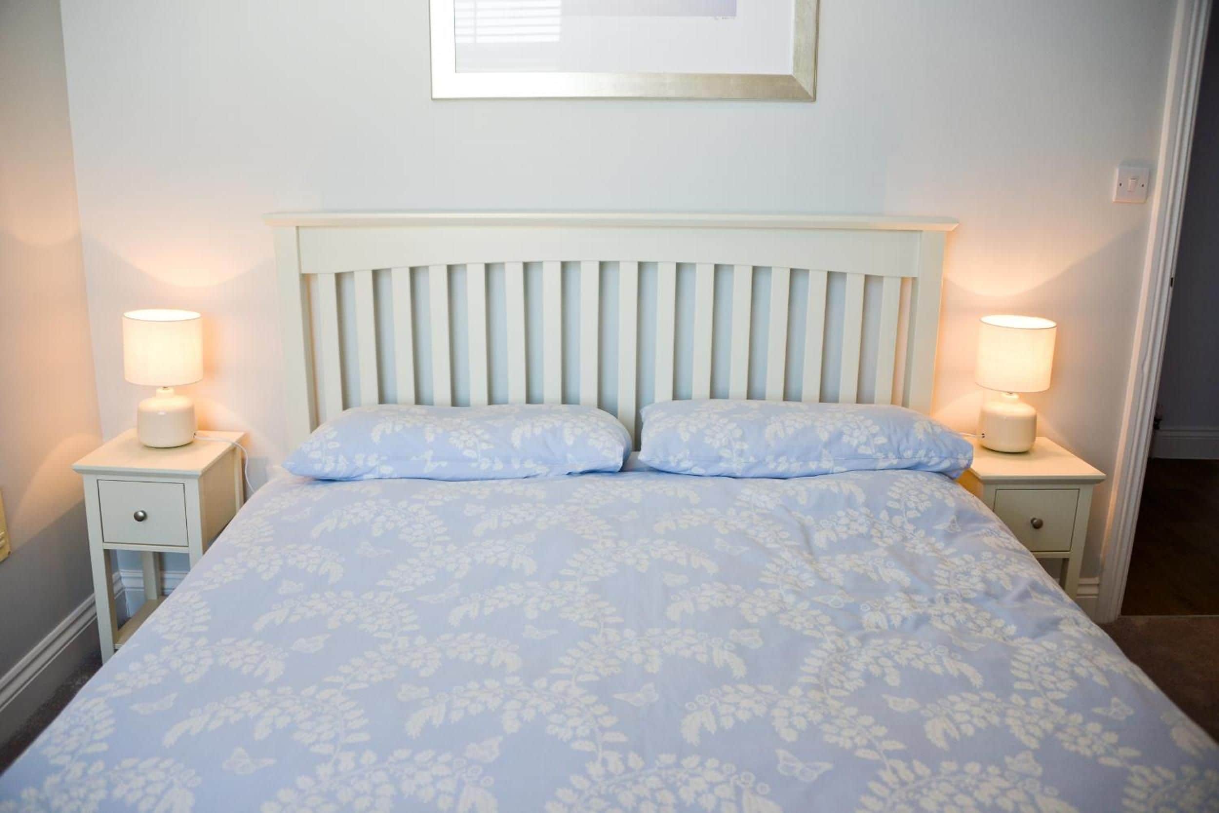 A bed with a headboard, two bedside tables with lamps, and a framed picture on the wall.