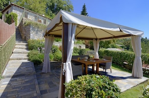 A covered outdoor seating area with a table and chairs, surrounded by stone steps and greenery.