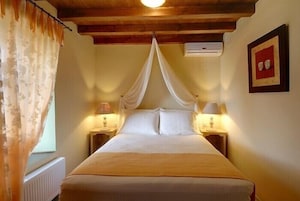 A bedroom with a canopy bed, two bedside lamps, a radiator, and a framed picture on the wall.