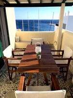 Una mesa de madera con cuatro sillas, una planta en maceta y vistas al mar y a los barcos.