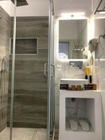 Un baño moderno con cabina de ducha de vidrio, tocador con espejo y secador de pelo montado en la pared.