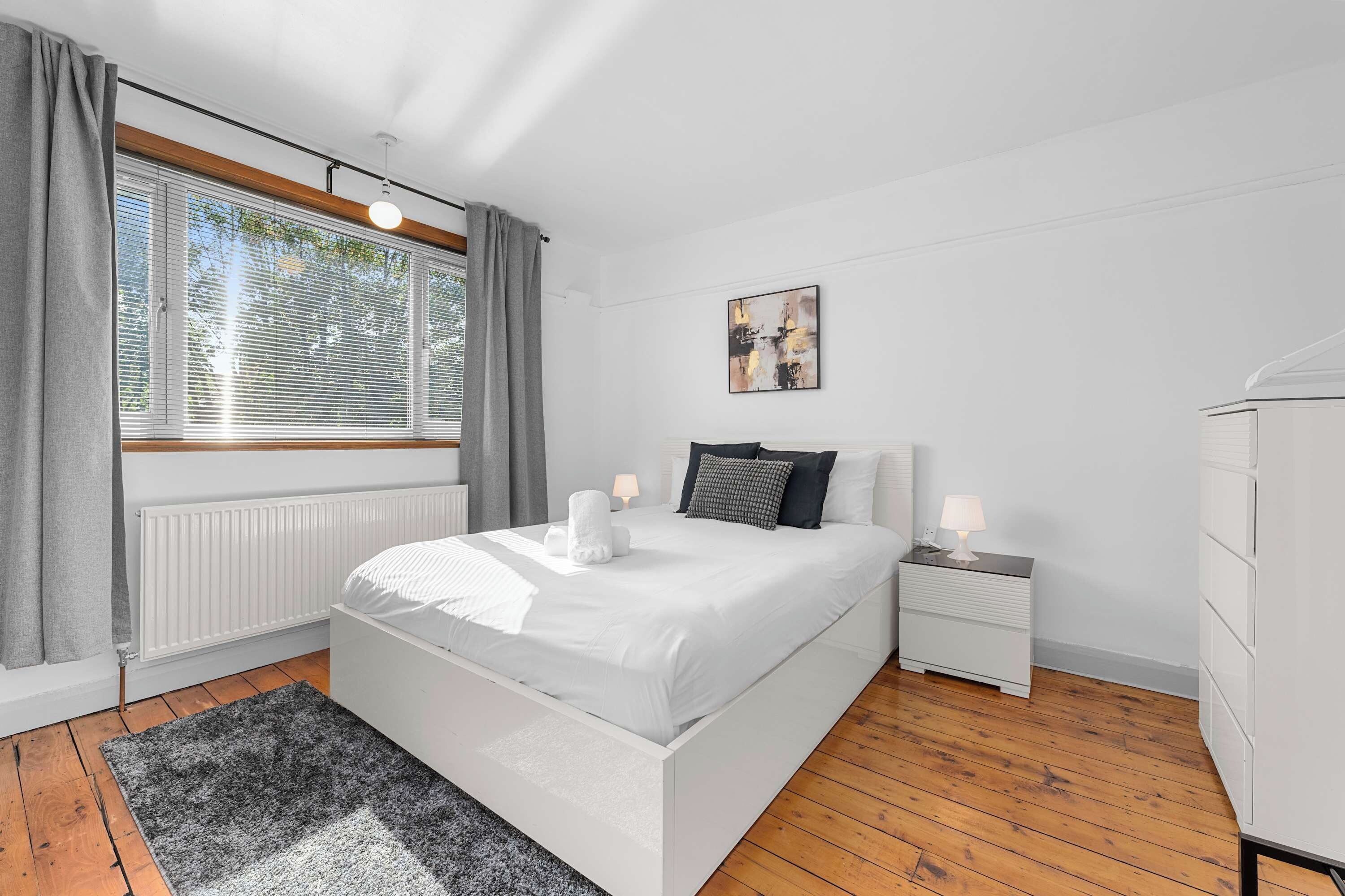 Une chambre moderne avec un grand lit, des lampes de chevet, un radiateur et une fenêtre avec des stores.