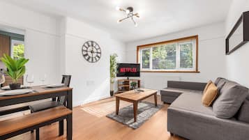 Een moderne woonkamer met een bank, een salontafel, een eettafel met stoelen, een televisie en een klok aan de muur.