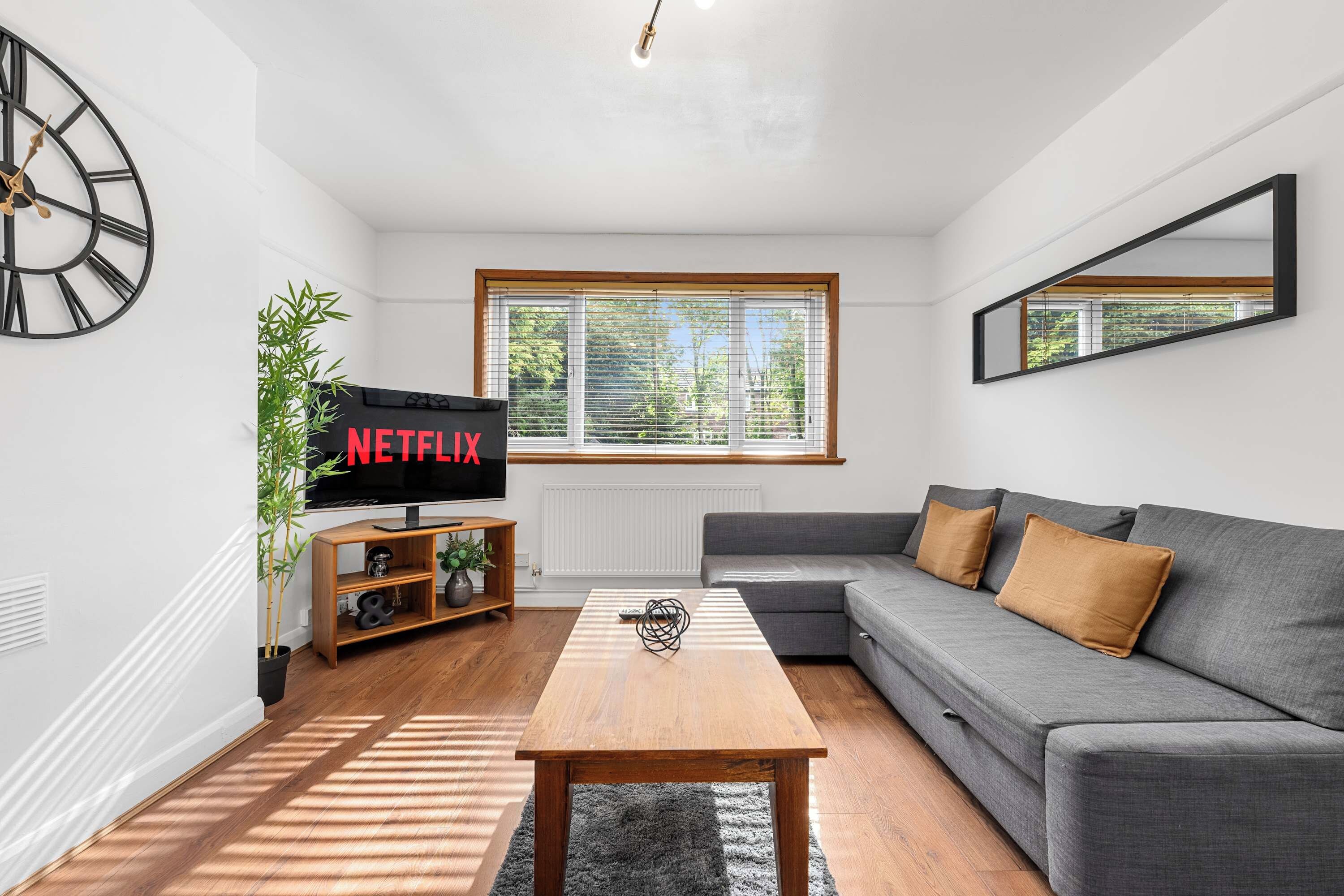 Un salon moderne avec un canapé gris, une table basse en bois et un téléviseur affichant le logo « NETFLIX ».