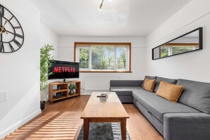 Un salón moderno con un sofá gris, una mesa de centro de madera y un televisor mostrando 'NETFLIX'.