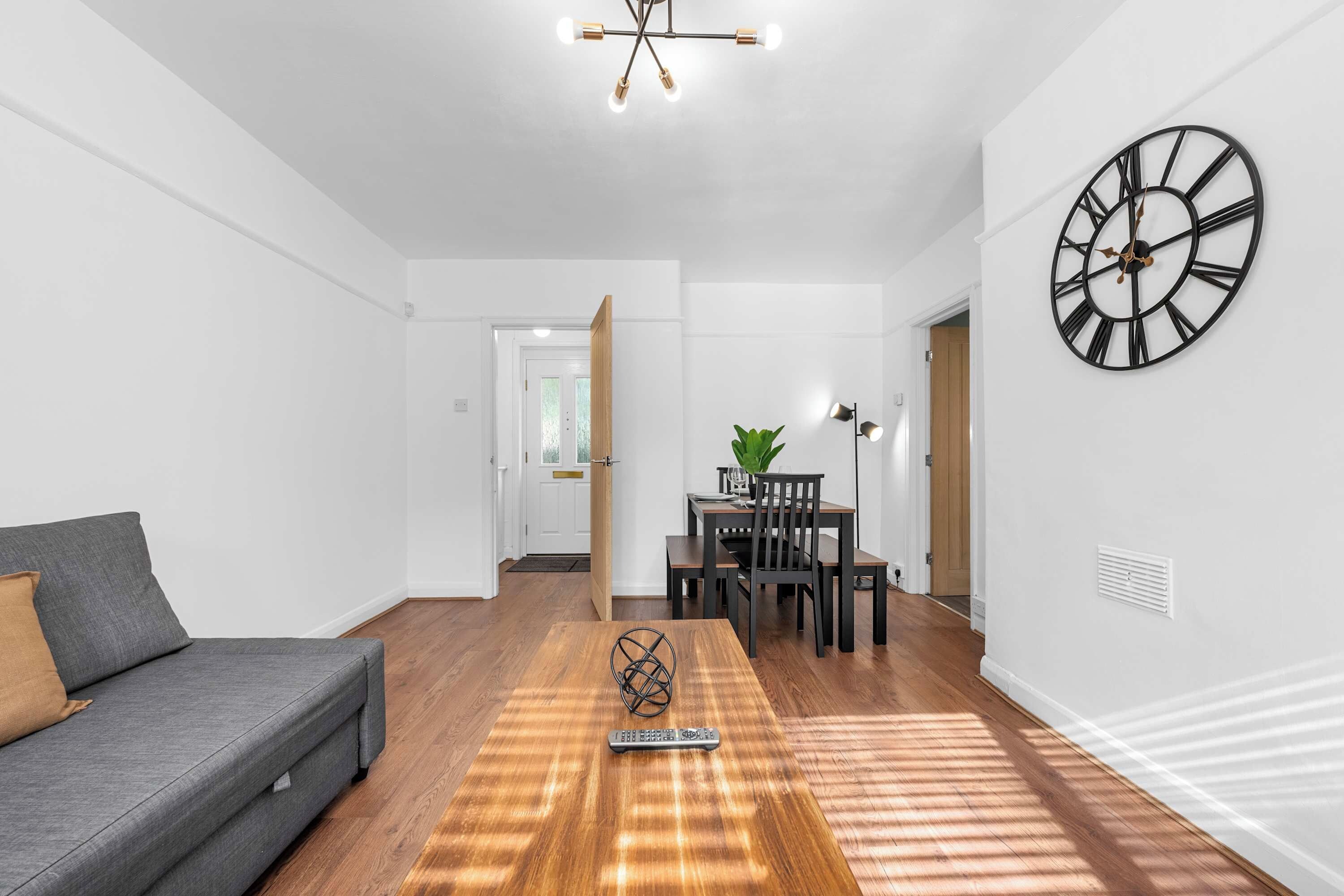 Un salon moderne comprenant un canapé, une table à manger avec des chaises, une grande horloge murale et un escalier menant à une autre pièce.