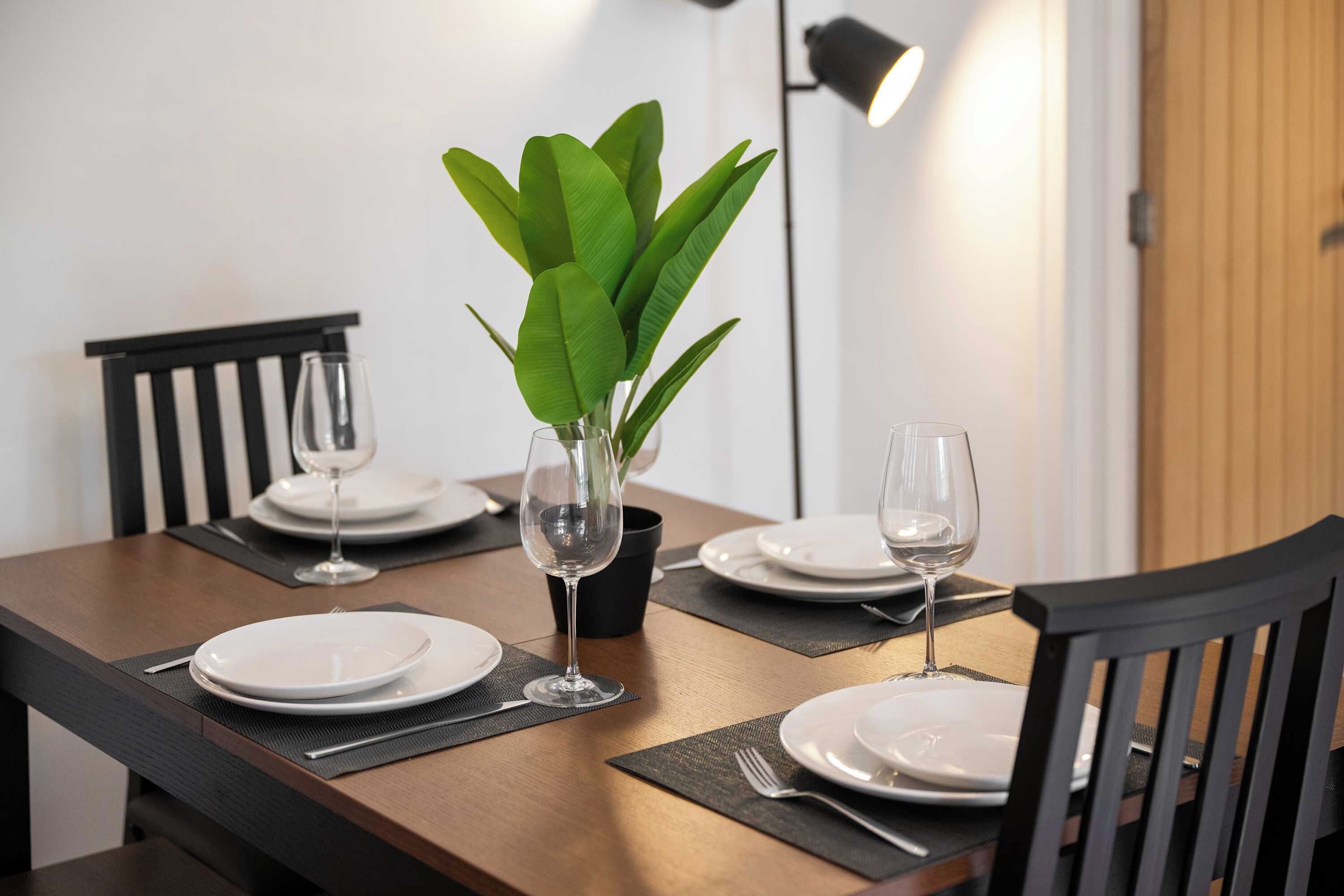 Een eettafel gedekt met borden, glazen en een potplant.