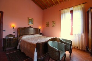 Un dormitorio con cama de madera, dos lámparas de noche, una mesita de noche, una silla, una ventana con cortinas y una puerta.