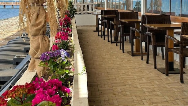 Un área de comedor al aire libre con mobiliario de mimbre y lámparas colgantes de ratán, con vistas a una masa de agua.