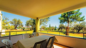 Un espacio al aire libre techado con mesa y sillas, vista a árboles y a un área con césped.