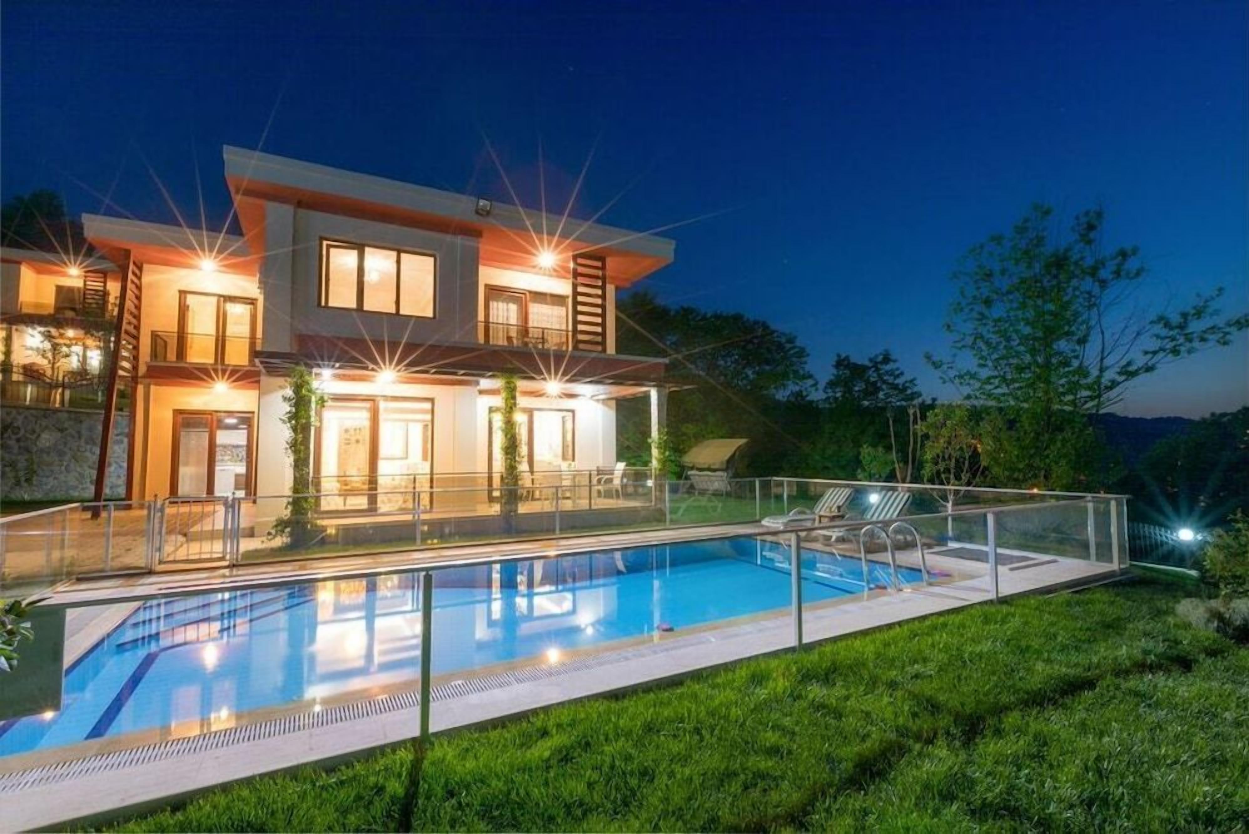 Une maison moderne à deux étages, dotée d’une piscine, de mobilier d’extérieur et d’un éclairage extérieur soigné.