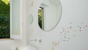 Casa de banho com uma pia branca, dois espelhos e azulejos decorativos.
