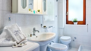 Un baño con lavamanos, inodoro y bañera. Hay toallas y artículos de aseo en el lavamanos.