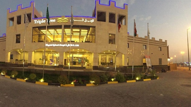 A hotel with a central entrance, multiple flags, and a well-lit facade. - Triple Tree Hotel (Al-Hofuf)