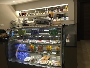 A food display case with various snacks and drinks, a coffee machine, and shelves with bottles in a hotel setting.