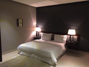 A neatly made bed with white linens, two bedside tables with lamps, and a small wall art piece. - Triple Tree Hotel (Al-Hofuf)